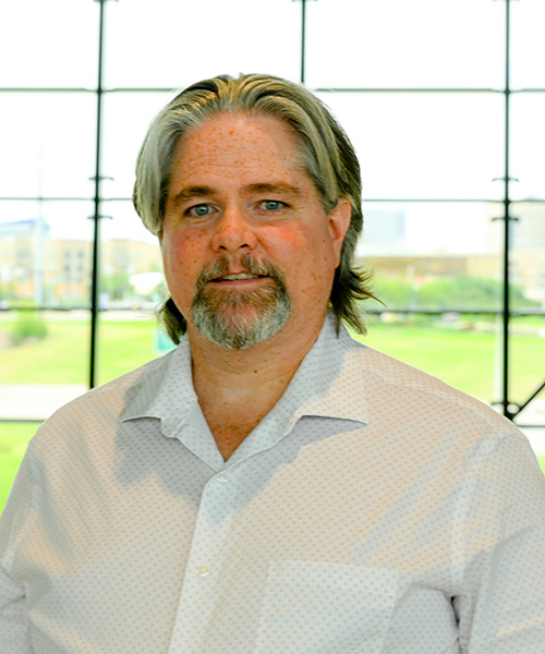 Headshot of older gentleman with gray hair standing in front of a large window backdrop