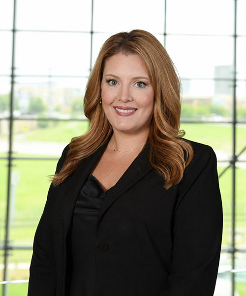 Headshot of red headed woman in black standing in front of a large window backdrop