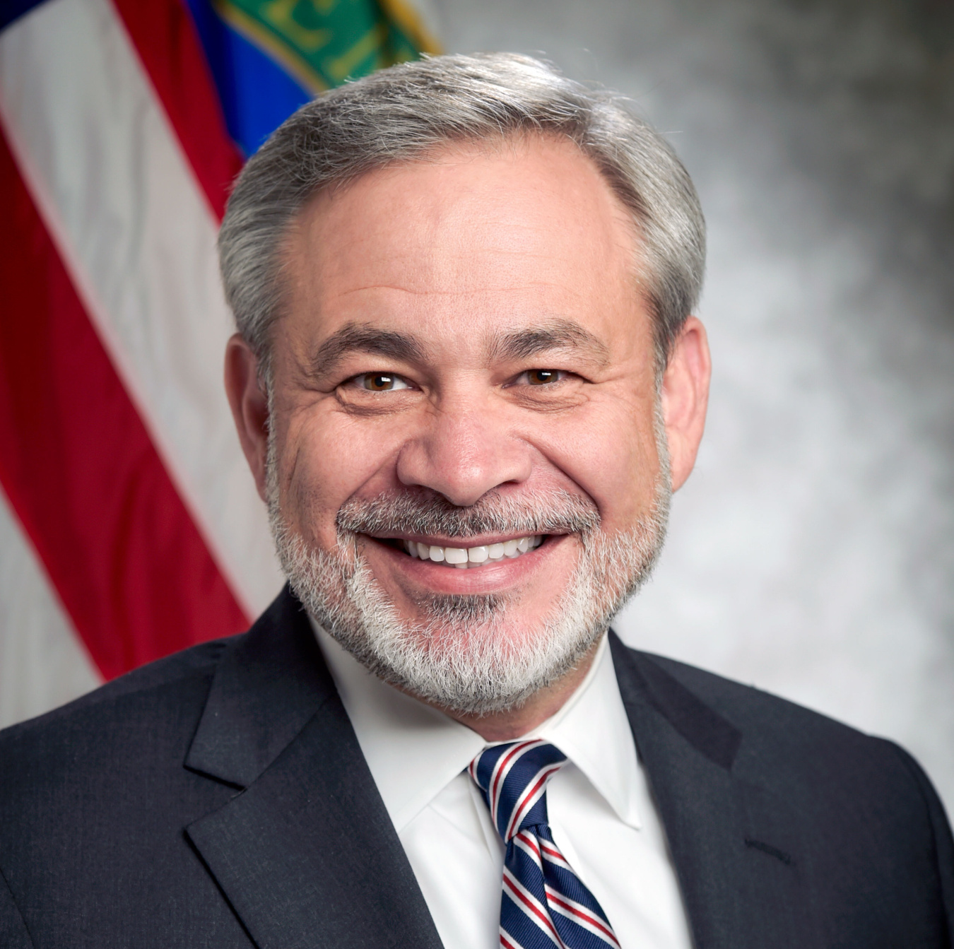 Dan Brouilette Headshot of gray haired man in suit with American flag background