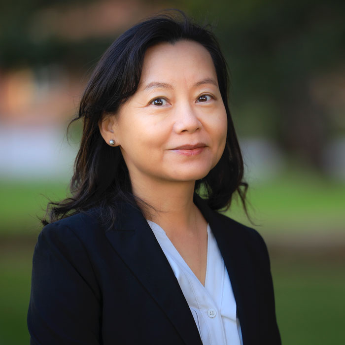 lixia_lambert.jpg Headshot of dark haired woman in white blouse and black blazer with blurred outdoor background